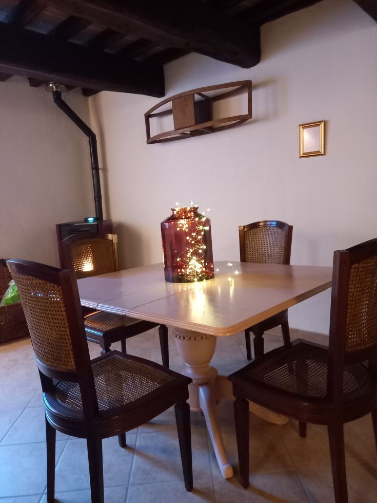 Un tavolo con sedie in un contesto rustico, illuminato da luci in un ambiente caldo e accogliente.