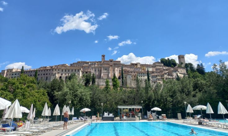 Scena di un borgo in estate con una piscina, sotto un cielo sereno e soleggiato.