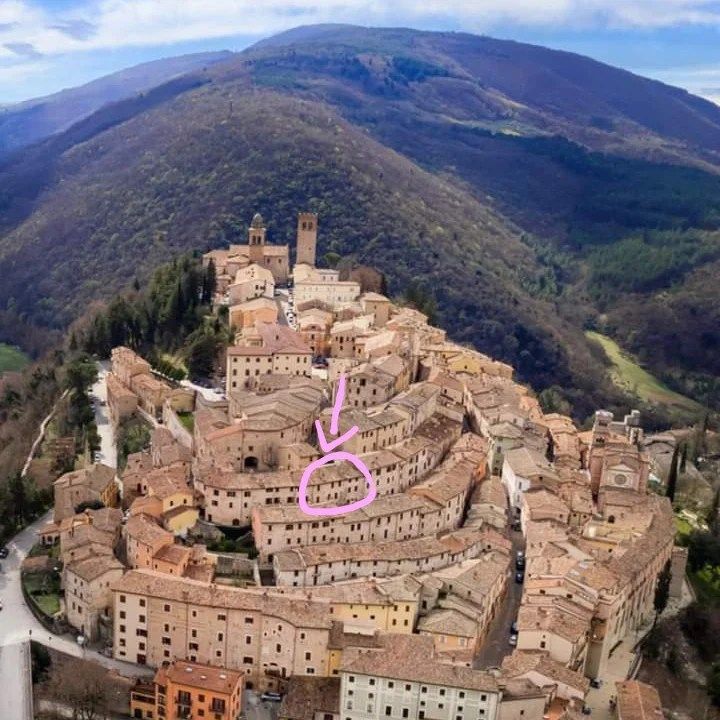 Panorama di un antico borgo medievale circondato da verdi colline.