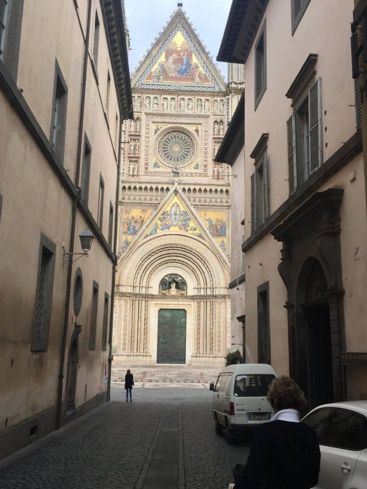 Panorama del Duomo di Orvieto adagiato su una strada in pietra, circondato da edifici storici.