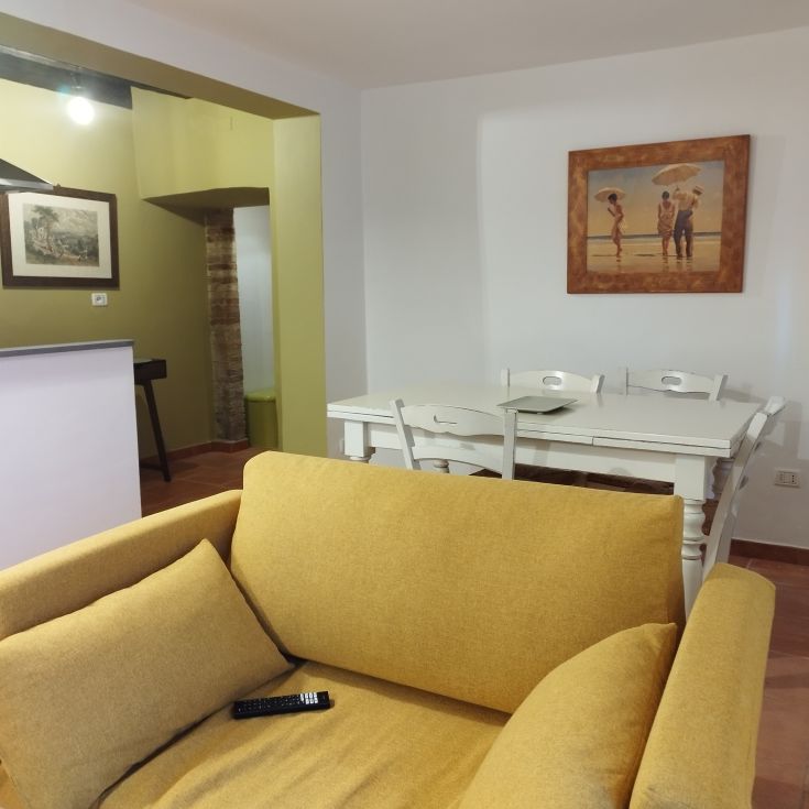 Soggiorno luminoso con divano giallo e tavolo bianco, arredato in modo semplice e rilassante.