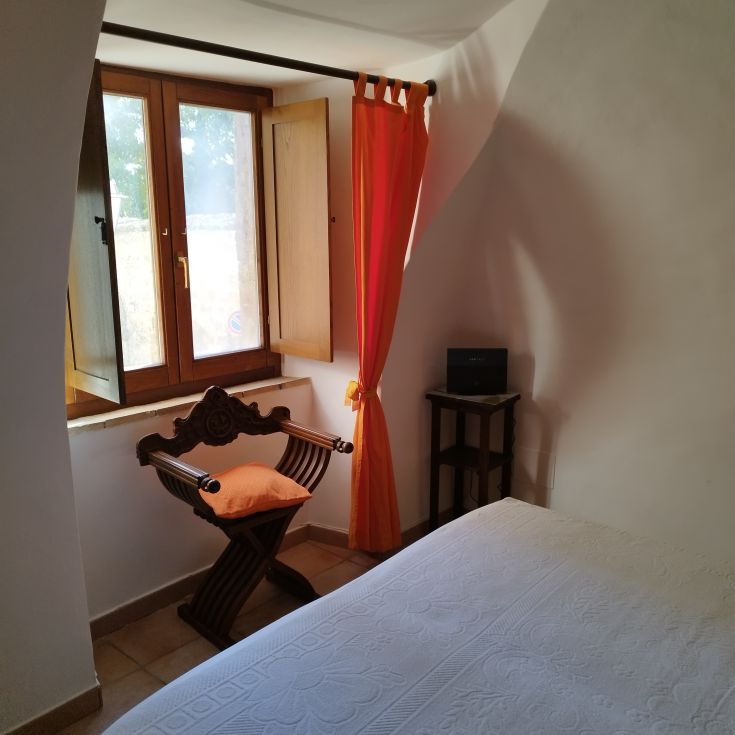 Uno spazio interno semplice con una finestra aperta, tende arancioni che diffondono luce nella stanza.