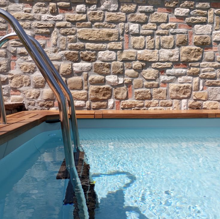 Ein ruhiger Swimmingpool mit einer Metallleiter und einer Steinmauer im Hintergrund.