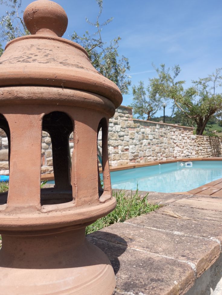 Eine Terrakotta-Lampe steht neben einem Pool, der von natürlicher Vegetation umgeben ist.