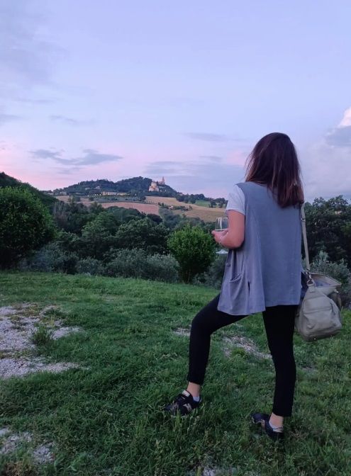 Eine Person betrachtet eine Landschaft mit sanften Hügeln und einem kleinen Dorf, das im Sonnenuntergangslicht erstrahlt.