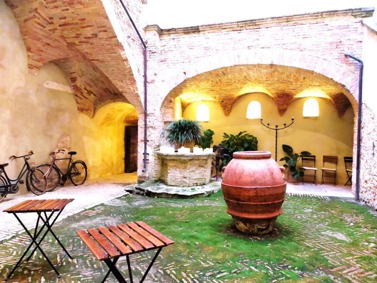 A simple courtyard featuring a large vase and parked bicycles, adorned with arches and green plants.