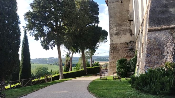 A pathway among trees and historic walls, surrounded by the greenery of the Umbrian countryside.