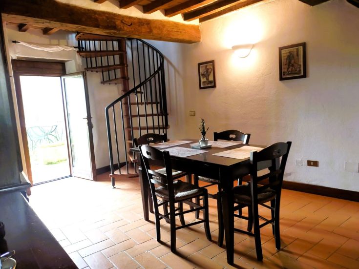 Interior of a building with a table and spiral stairs. Simple details and natural light create a cozy atmosphere.