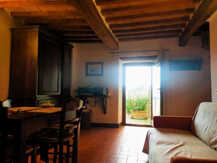 A peaceful living room with simple furniture and a door leading to a garden. Relaxed atmosphere.