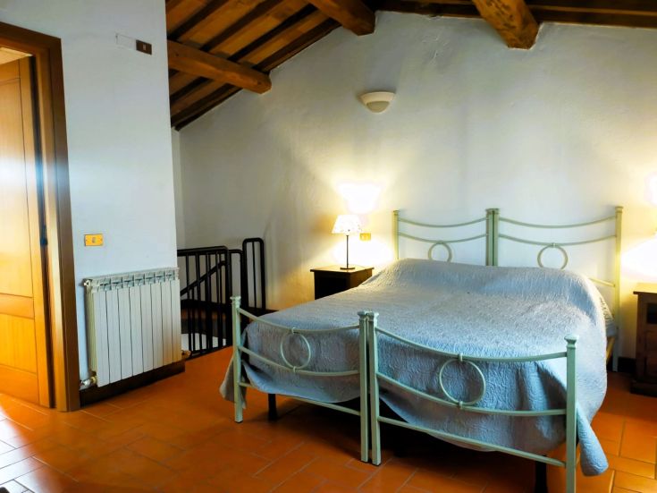 Simple bedroom with rustic wood beds, illuminated by nightstand lamps and featuring terracotta flooring.