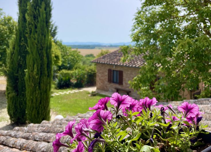 Un casale circondato da vegetazione, con fiori variopinti e panorami sulle colline circostanti.
