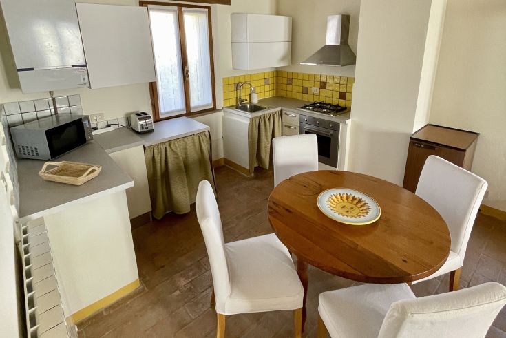 Cucina semplice e luminosa con un tavolo per pranzi e cene conviviali al Casale dell'Assiolo.