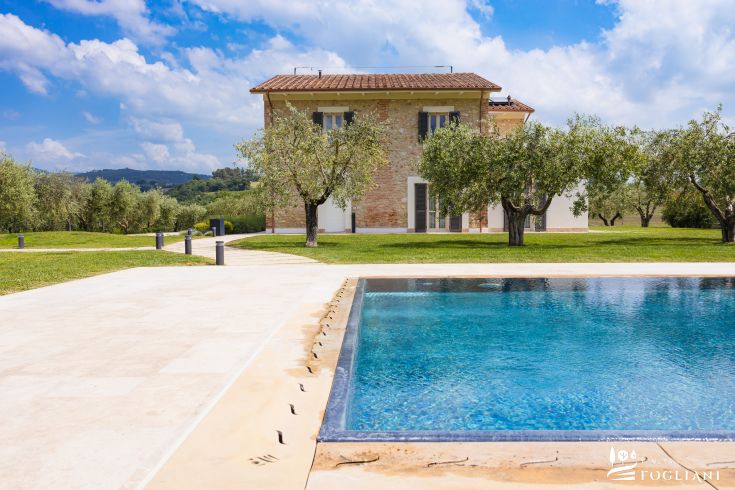 Une villa avec piscine située dans la campagne ombrienne, entourée d'arbres et de végétation luxuriante.