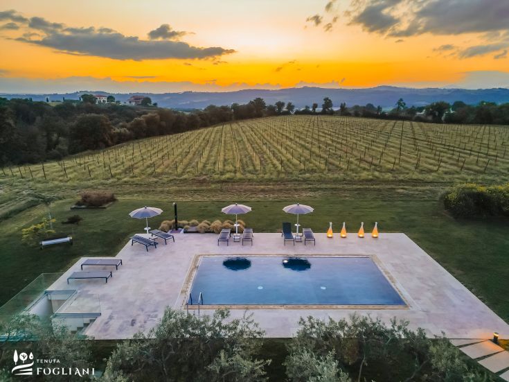 Vue de la Tenuta Fogliani avec piscine et vignobles au coucher du soleil.