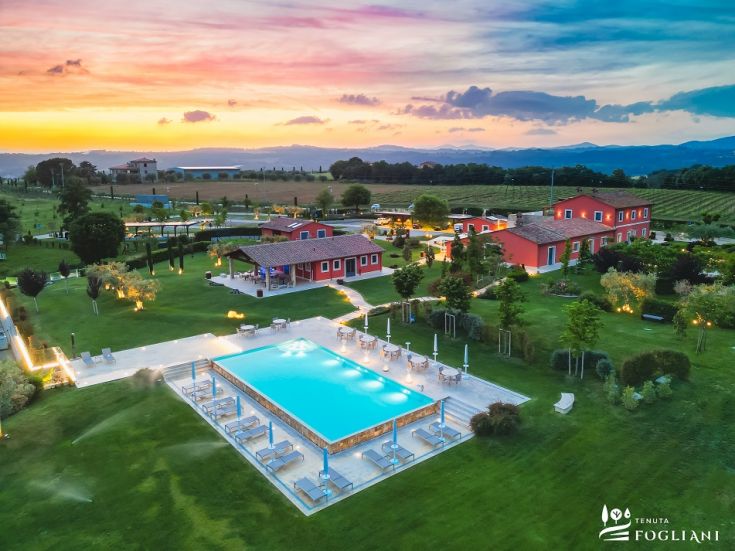 La Tenuta Fogliani au coucher du soleil, entourée de verdure luxuriante et avec une piscine visible.
