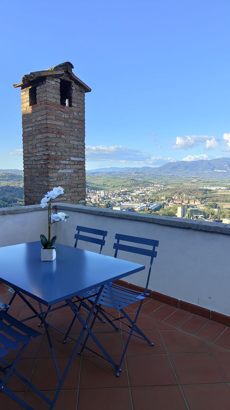 Terrasse surplombant Narni avec une table bleue et une vue imprenable sur la vallée environnante.