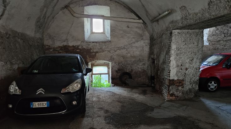 Un garage avec des murs rustiques, des véhicules à l'intérieur et des fenêtres montrant une végétation verte.