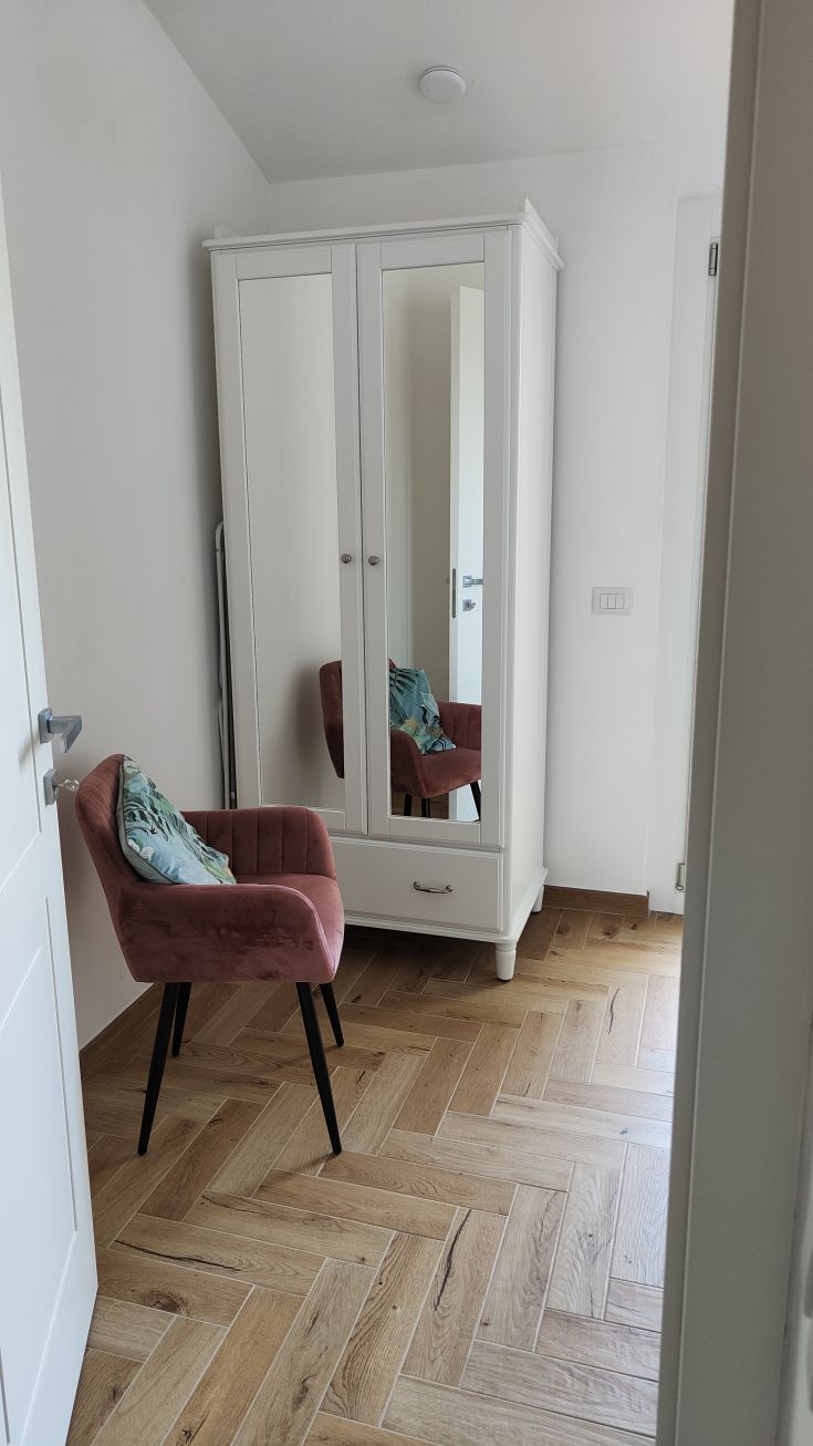 Chambre simple avec une armoire et un fauteuil, avec un sol en bois et une lumière naturelle.