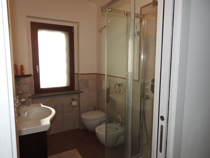 Interno di un bagno luminoso con doccia, lavabo e sanitari semplici.