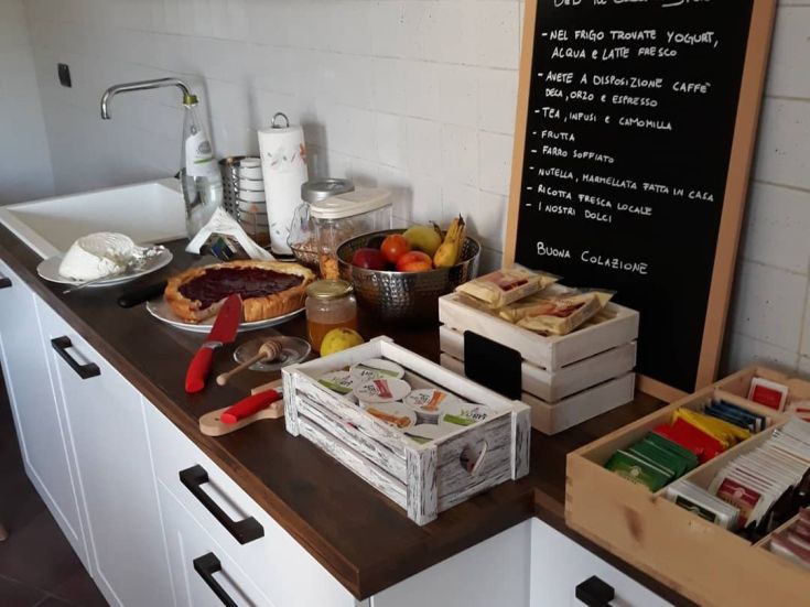 Colazione ricca con pasticcini freschi, frutta di stagione e bevande calde servita in una cucina accogliente.