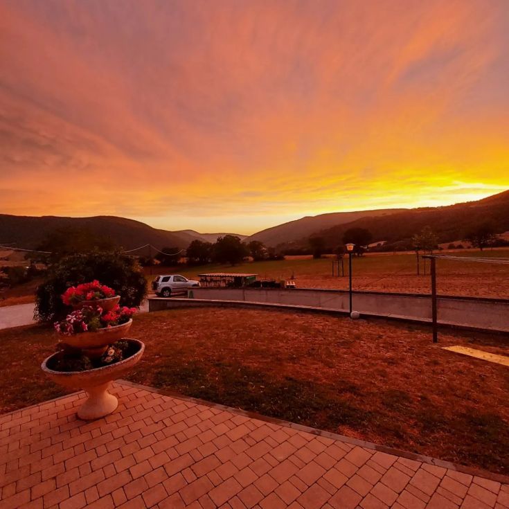 Tramonto sulle colline con un giardino fiorito in primo piano.