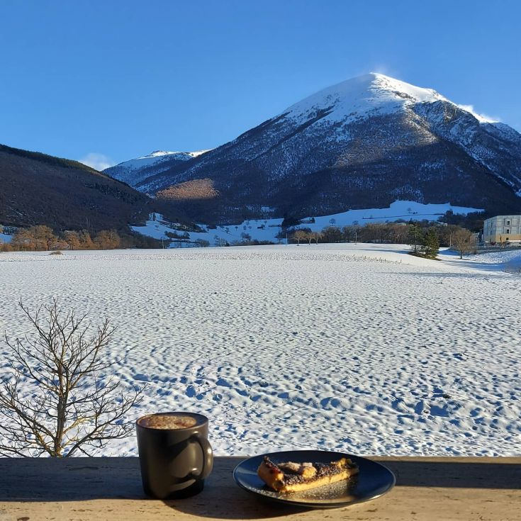 Una scena invernale tranquilla, con montagne sullo sfondo, una tazza di cioccolata calda e una fetta di torta.