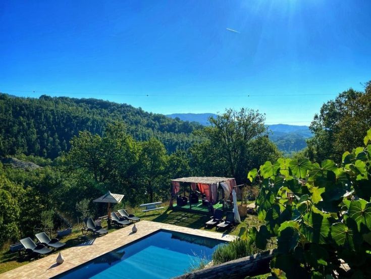 A scene of a farmhouse with a swimming pool, surrounded by gentle green hills.