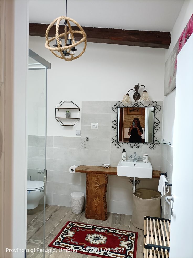 A modern bathroom with a stone sink and simple decorations. It features a red rug and functional details.