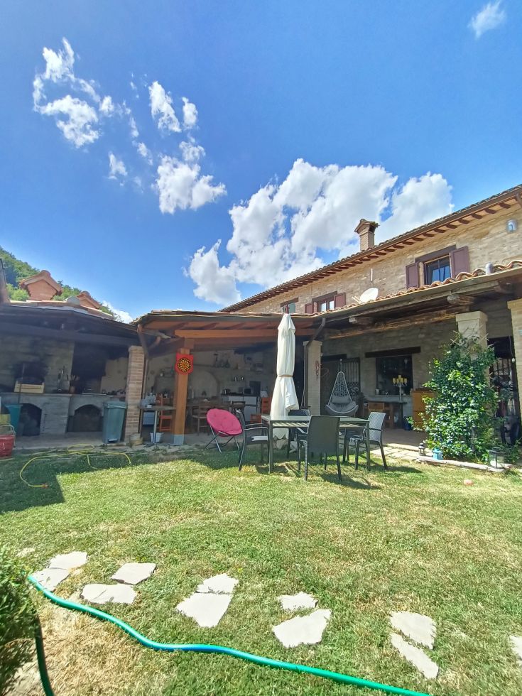 A stone building surrounded by a garden and some outdoor benches, under a clear sky.