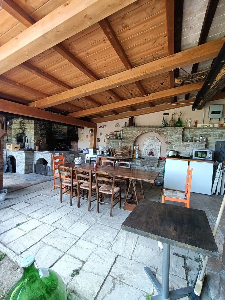 Inside a building, featuring a wooden table, functional kitchen, and a fireplace.