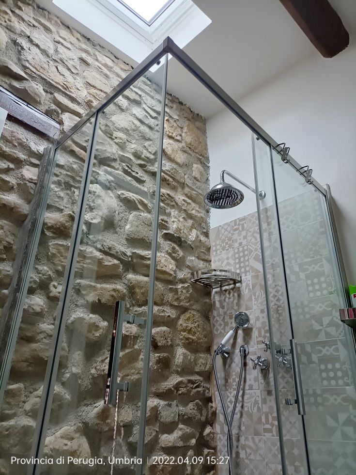 A simple stone shower in a bathroom with stone walls, illuminated by a window above.