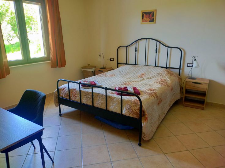 Spazio intimo con un letto matrimoniale e una scrivania, ben illuminato da finestre che si affacciano su un'area verde.