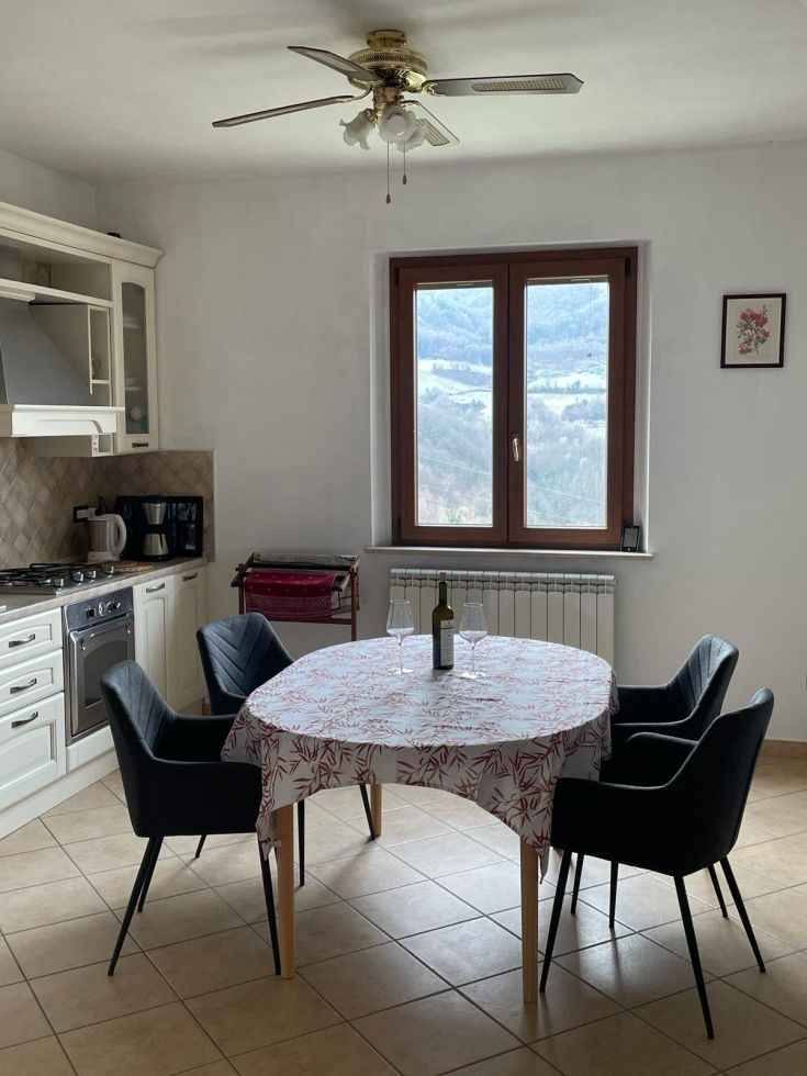 Cucina semplice con tavolo e sedie, un bicchiere di vino e panorama sulla natura circostante. Un angolo di relax.