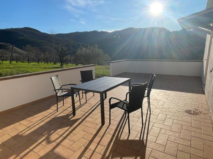Ampia terrazza soleggiata con panorama sulle colline, arredata con un tavolo da pranzo accogliente.