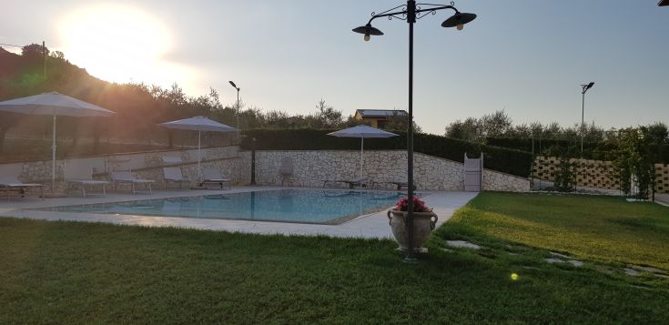 A pool surrounded by trees and sun loungers, under the sunset sky.