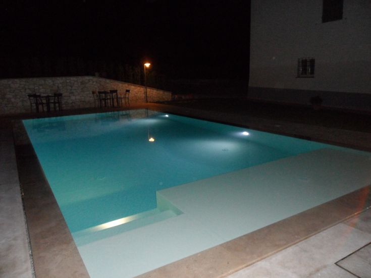 An illuminated swimming pool at night, surrounded by outdoor furniture, exuding relaxation.
