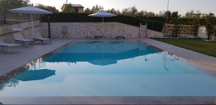A clear pool surrounded by greenery with sun loungers available for relaxation.