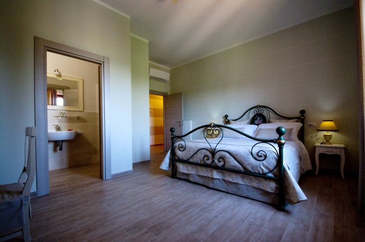 Simple room with wrought iron bed and separate bathroom, lit by natural light.