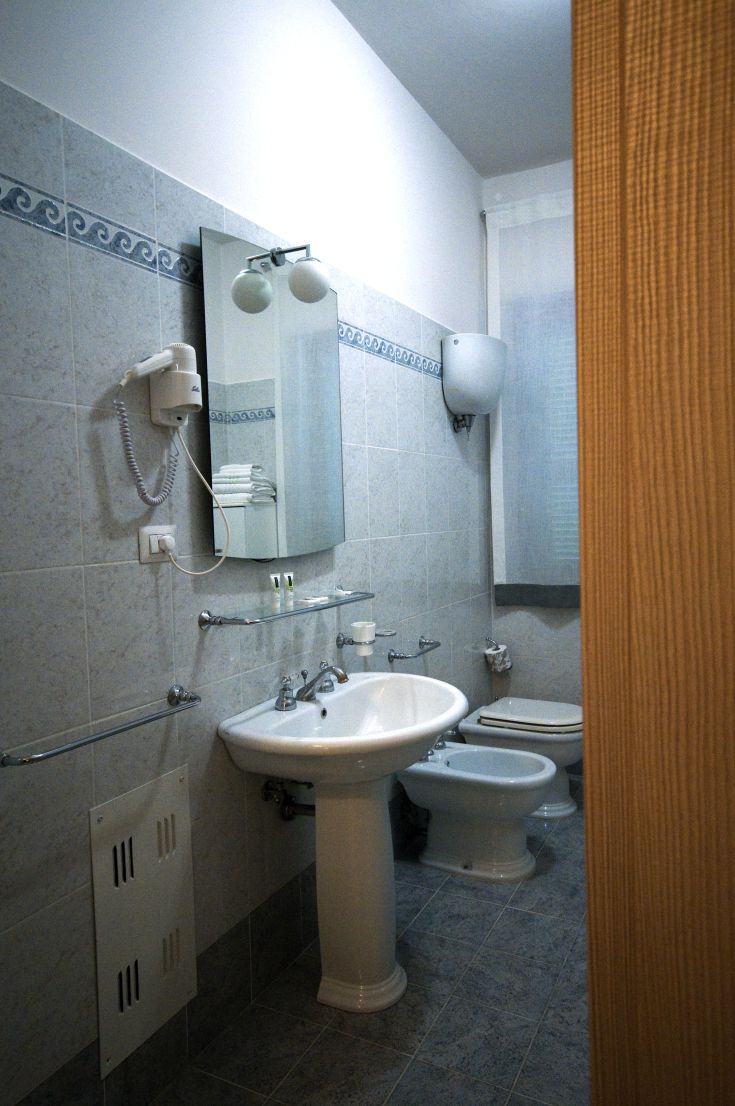 A modern bathroom featuring a sink, bidet, and a mirror. The decor is simple and functional.