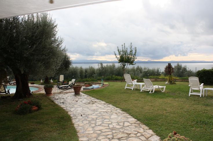 View of Lake Trasimeno, surrounded by olive trees and a well-kept garden.
