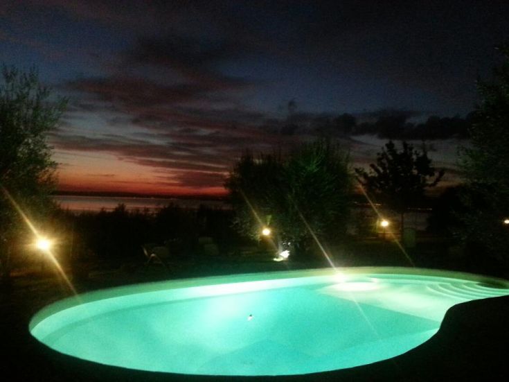 A lit outdoor pool under a sunset sky reflecting on the water. The setting is natural and tranquil.