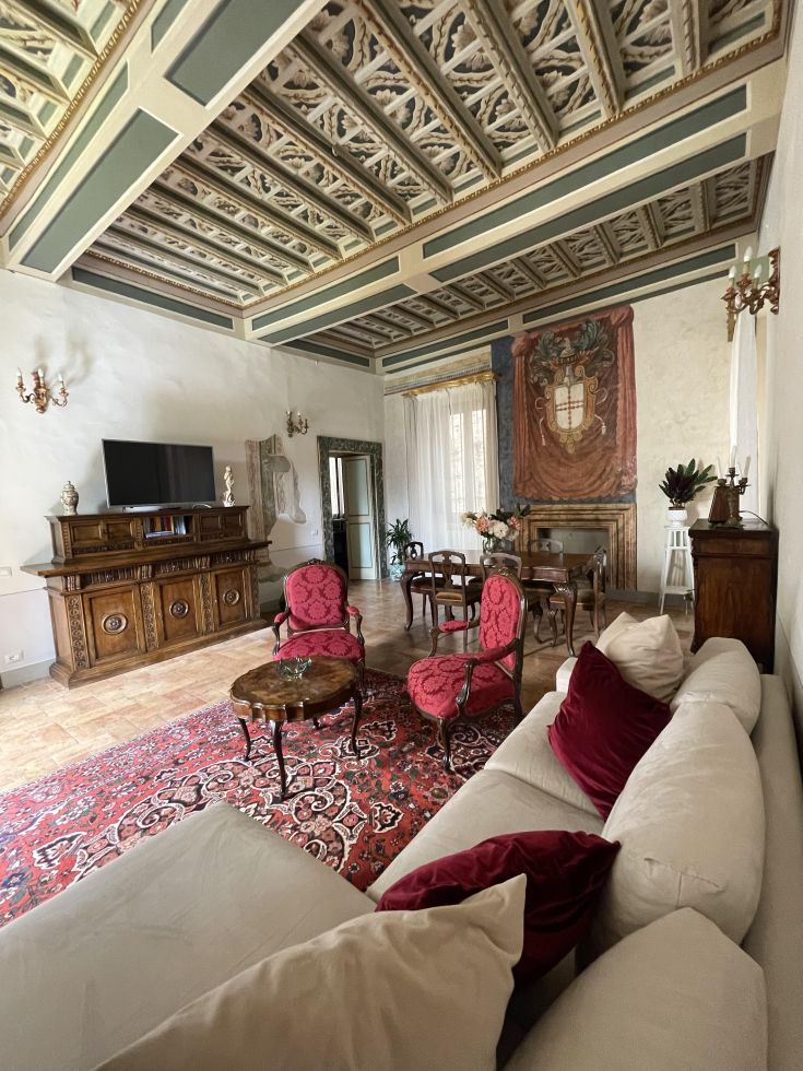 Ampio salone di un appartamento in un palazzo storico, con arredi semplici e decorazioni in stile classico.