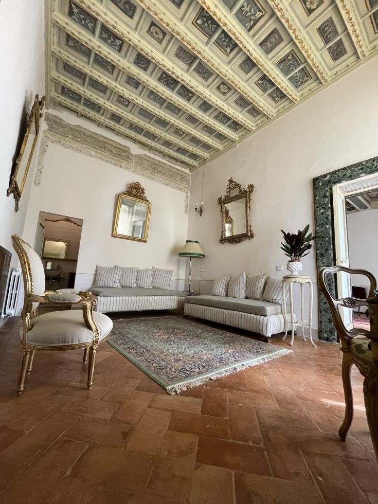 Interno di un palazzo con soffitti decorati, illuminato dalla luce naturale e arredato con mobili sobrii.