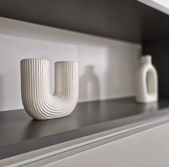 A white vase on a light wooden shelf, featuring a simple and modern design.