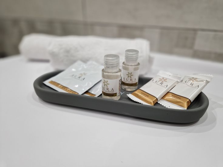 Bathroom accessories arranged on a gray tray, with white towels in the background.