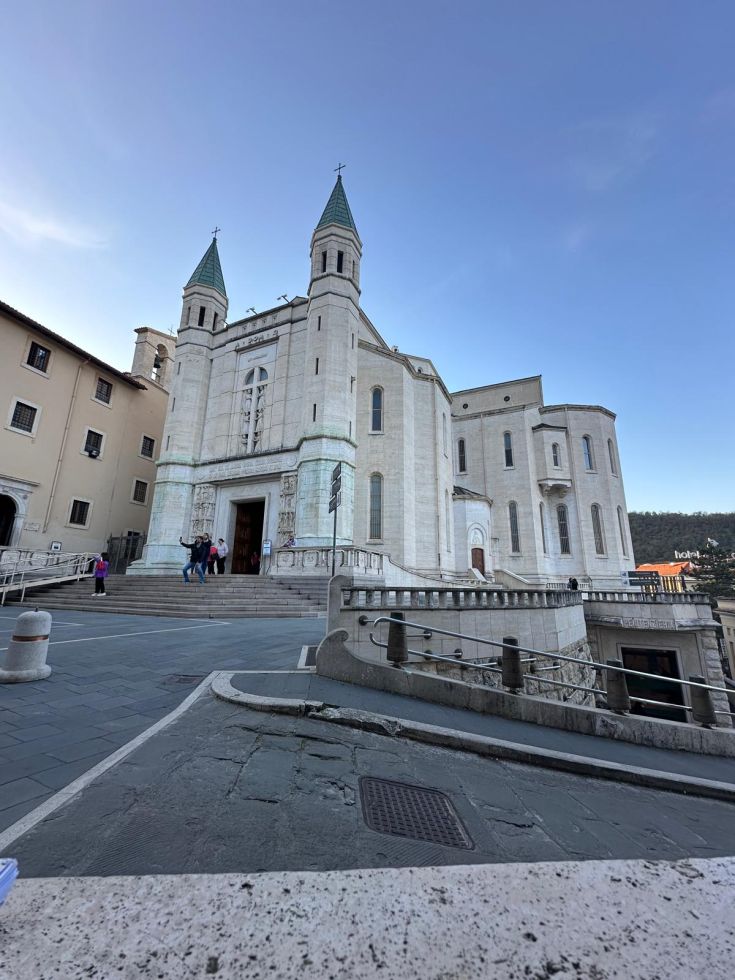 Edificio religioso con torri e facciata distintiva situato nel centro di Cascia, circondato da giardini e strade alberate.