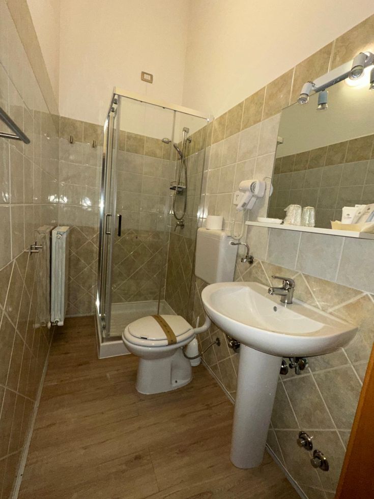 Bagno moderno con doccia, lavabo e elementi base, arredato in modo pratico e sobrio.