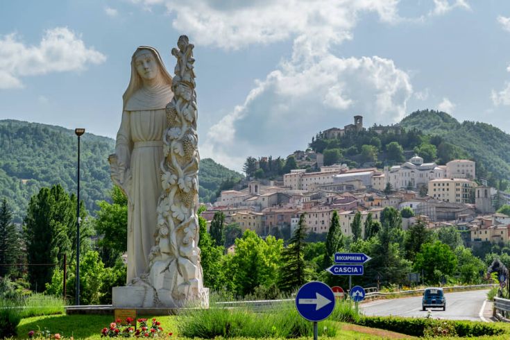 Una statua di dimensioni notevoli accoglie i visitatori all'entrata di Cascia, immersa nel verde circostante.