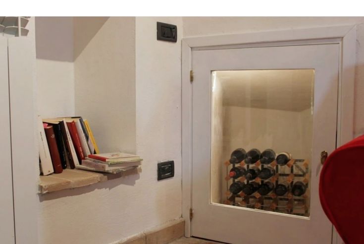 A cozy reading corner with a bookshelf and a wine cellar visible through a glass door.