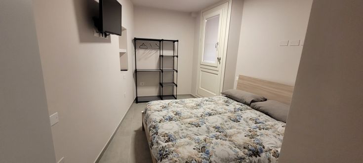 Camera semplice e luminosa con letto matrimoniale, TV e armadio, in un'atmosfera confortevole.